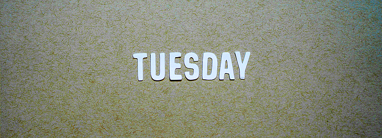 The word “Tuesday” in cutout paper letters on a textured background